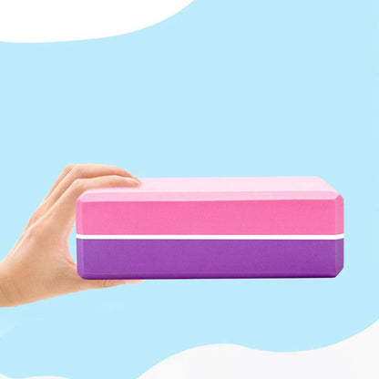 Two-color yoga brick held in hand against a light blue background.