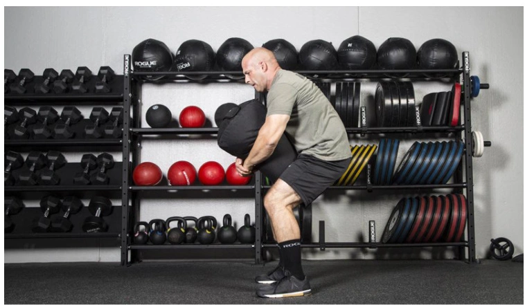 Man lifting fitness training weight-bearing sandbag in gym.