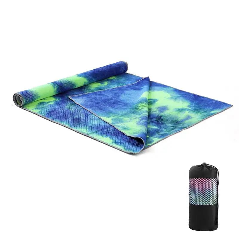 Tie-dye yoga blanket pad towel with vibrant blue and green pattern, rolled and accompanied by a net bag.