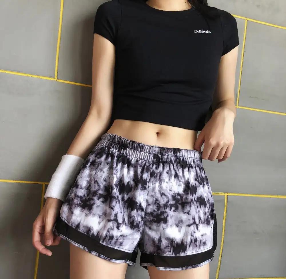 Yoga fitness short sleeve top in black worn by woman against tiled background.